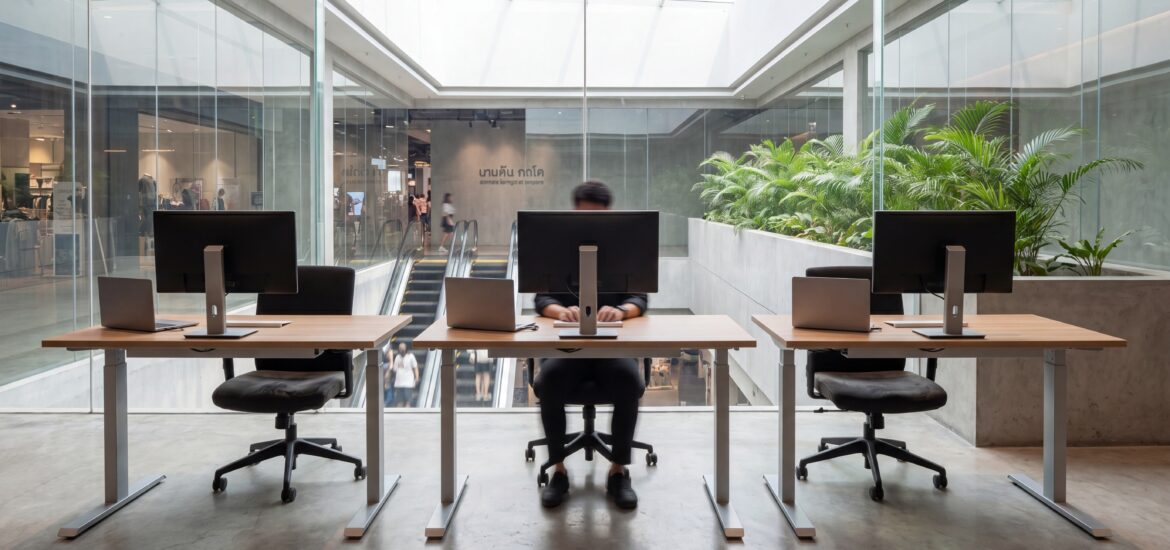 Free workspace area in a Bangkok mall with adjustable-height desks, external monitors, and natural daylight