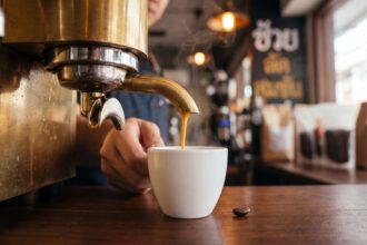 Espresso pour at a Bangkok specialty coffee bar with golden crema falling into a white ceramic cup and a brass machine