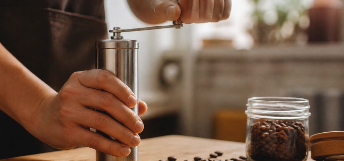 Hands grinding coffee beans with a stainless steel manual hand grinder