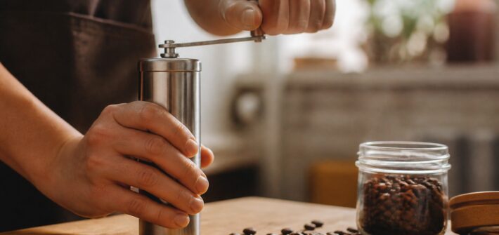 Hands grinding coffee beans with a stainless steel manual hand grinder